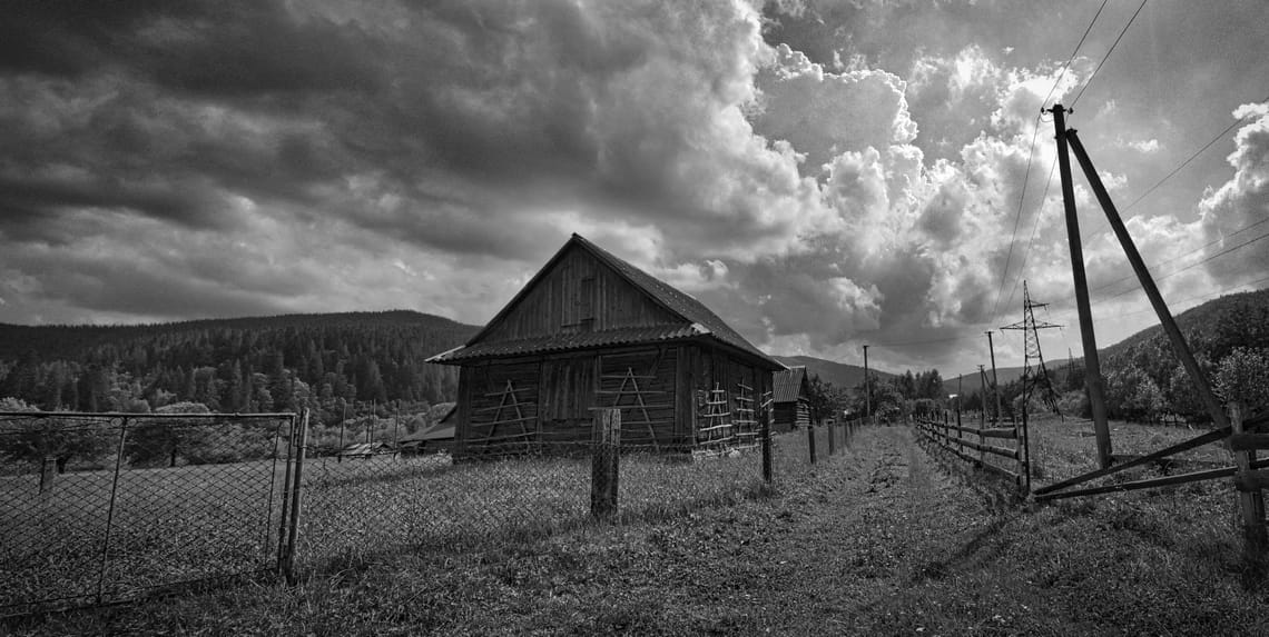 A wooden cabin in the foreground with mountains and electrical poles and towers in the background.