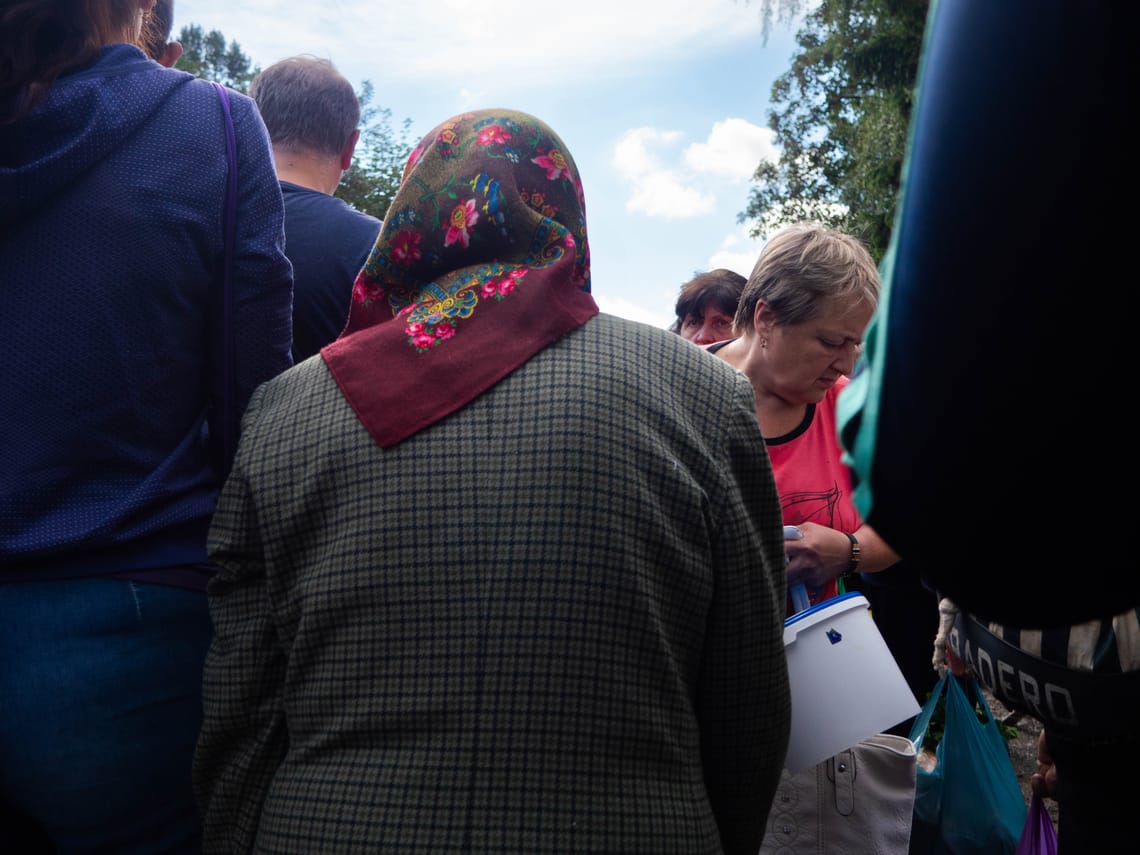 A shorter woman with a headscarf navigates a market surrounded by taller people.