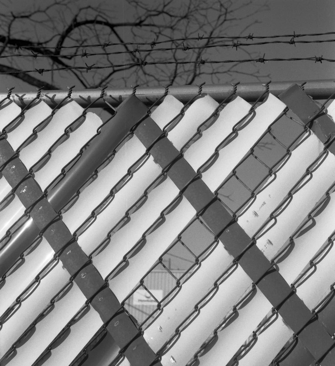 An industrial building peeking through a gap in a fence covered by geometric slats.