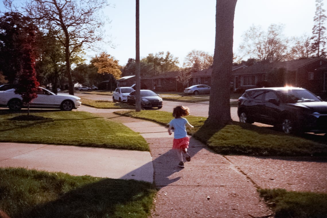 A child in a skirt running away from the camera down a side walk.