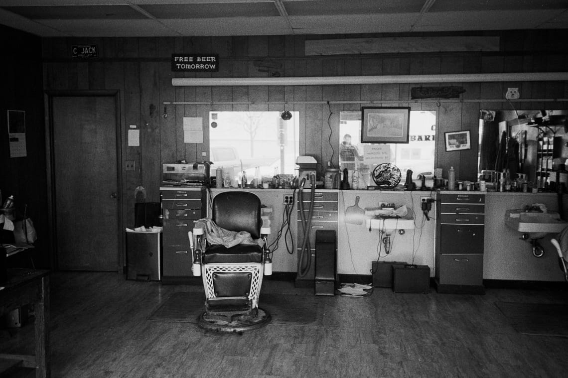 An empty barbershop, chair visible in the foreground with a sign saying "Free Beer Tomorrow" in the background.