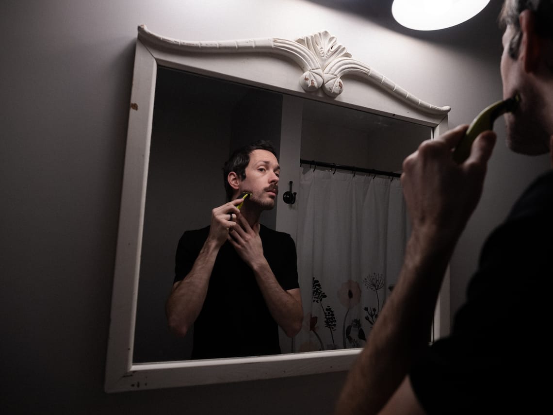 A self portrait of the photographer using an electric shaver. The camera is pointed at the mirror focused on his reflection.