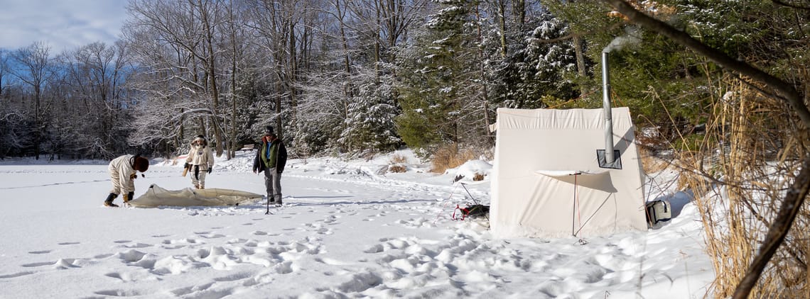 Left: Three people on a frozen lake set up a hot tent on the ice. Right: An erected hot tent with smoke coming out of the chimney.